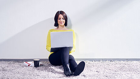 Frau sitzt mit einem Laptop an der Wand und besucht die ibo Website 