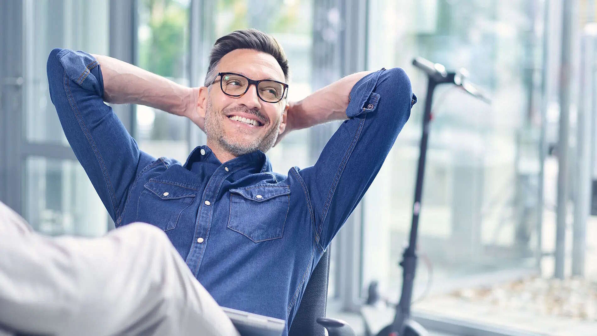 Zukunft organisieren mit ibo Männliche Person sitzt mit verschränkten Armen hinter dem Kopf lächelnd auf einem Stuhl